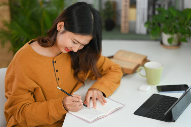 istock Pretty young Asian woman making important notes while planning daily appointment at her work desk. 1906483140