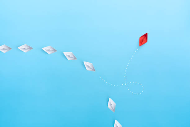 istock Group of white paper ship in one direction and one red paper ship pointing in different way on blue background. New idea, Unique way and Business for innovative, solution concepts. 1906489332