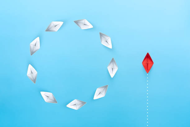 istock Group of white paper ships float in a circular direction and one red paper ship pointing in different way on blue background. Business for new ideas creativity, innovative and solution concept. 1906489335