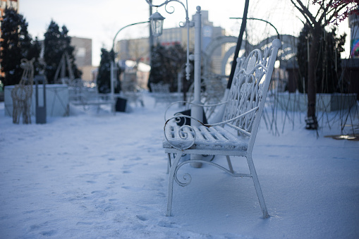 White park bench covered with ice and snow. Frozen park for lovers in severe frost and cold temperatures