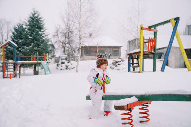 menina balança em um balanço coberto de neve no parquinho - playground snow winter little girls - fotografias e filmes do acervo