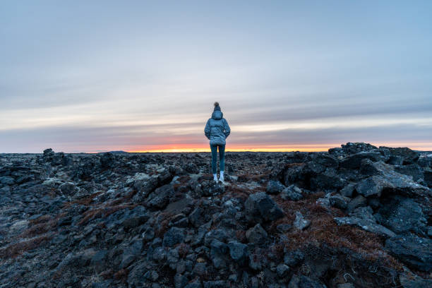 istock a person standing on some rocks watching the sunset over the ocean 1906540133