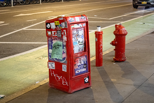 ny, United States – December 25, 2023: A red newspaper vending machine and a fire hydrant on a city street in New York