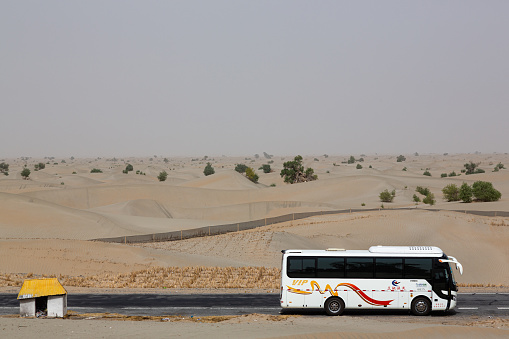 Kuqa, China – July 22, 2018: A large charter bus driving down a long, winding road in the Taklamakan Desert