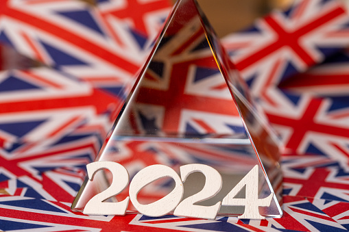 2024 the year twenty twenty four in wooden letters leaning against a crystal pyramid with the background of Union Jack paper strips