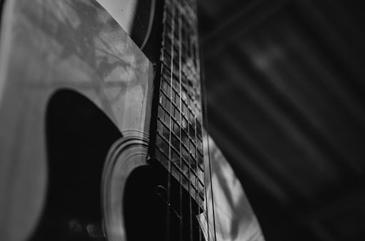A beautiful grayscale shot of an acoustic guitar leaned on a wooden door on a wooden surface