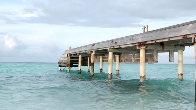 Wooden pier in the Caribbean sea with cloudy blue sky background.