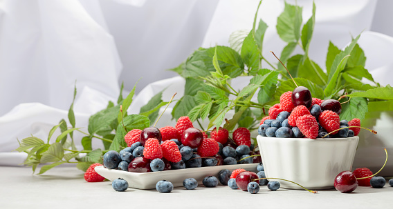Berries with leaves on a white table. Colorful assorted mix of blueberries, raspberries, and sweet cherries.