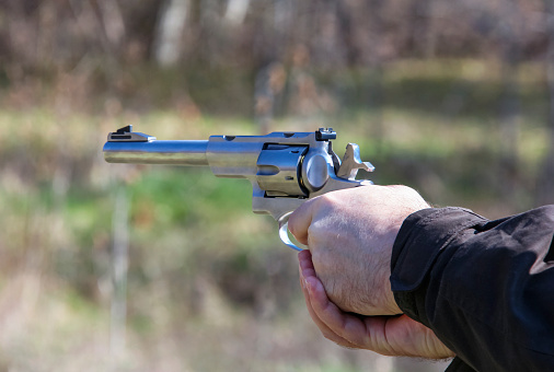 Short-barreled silver-colored weapon during shootout with left-handed man at shooting range. Pistol with revolver magazine in the hands of left-handed shooter before firing.