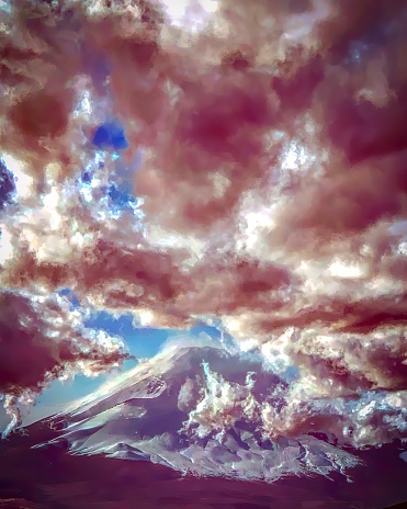 This photograph captures a majestic view of a mountain, likely Mt. Fuji, enveloped by a dramatic array of clouds under a sky tinged with a purple hue.