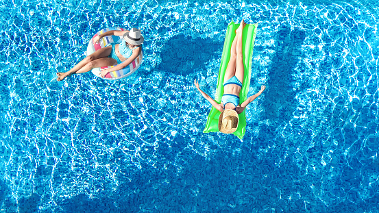 Young girls in swimming pool aerial drone view from above, happy kids swim on inflatable ring donut and mattress, have fun in water on family vacation on holiday resort