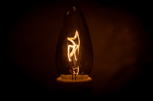 A light bulb glows brightly against a dark background, emitting a warm light