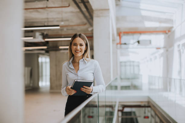 istock Young woman with notebook standing in the modern office hallway 1906771477