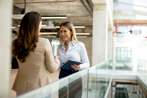 Two pretty young business women with paper notebook in the office hallway