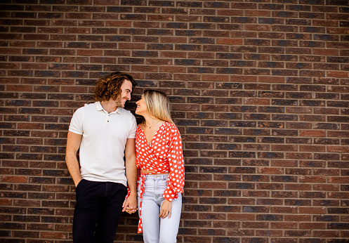 Handsome ymiling young couple in love in front of house brick wall