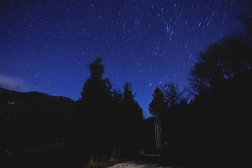 Wide panoramic view of the blue and cold starry night sky, seen from a dark and wild Slovenian mountain environment, at the beginning of winter season