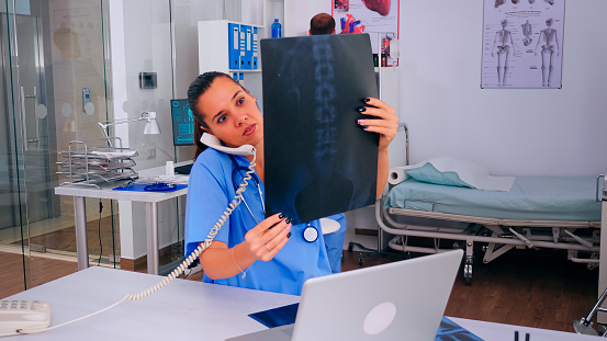 Nurse receptionist answering at hospital call checking the result of patient x-ray and diagnosing him. Healthcare physician in medicine uniform, doctor assistant helping with phone concultation