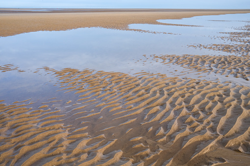 Still water reflects the sky and wet sand ripples like waves