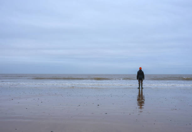 un homme seul se tient sur la plage en regardant la mer dans le nord du norfolk - north norfolk photos et images de collection