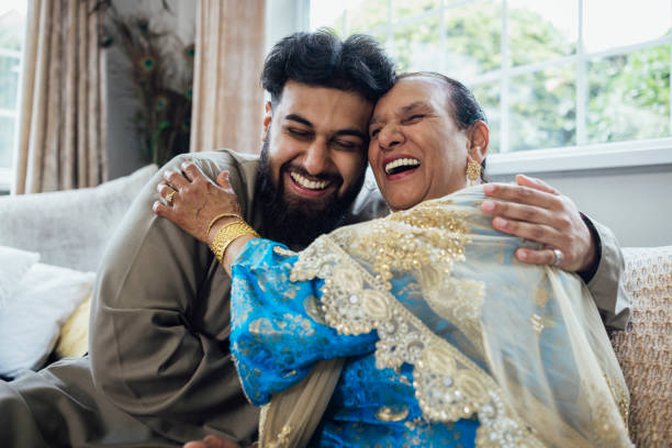 Feeling On Top of the World A shot of a grandmother and her grandson embracing whilst sitting on the sofa, both smiling broadly. They are gathered together with family for Eid celebrations at home in Middlesbrough, North East England. They are dressed in traditional outfits for the occasion. typical average stock pictures, royalty-free photos & images