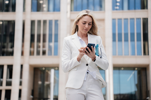 Elegant businesswoman in a white suit focused on her smartphone in an urban setting