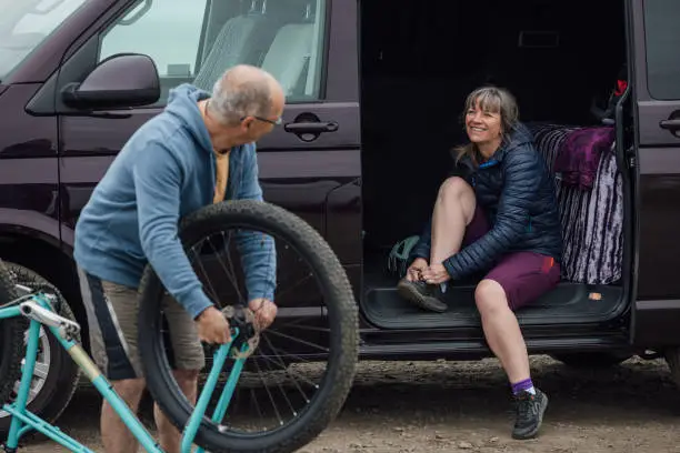 A mature couple wearing mountain biking sports clothing on an overcast day in Alnmouth, Northumberland, Northeastern England. They are getting prepared at their campervan for a day out on their mountain bikes.
