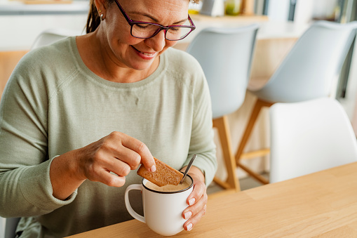 Close up of woman diping a cracker in hot drink cappuccino at home