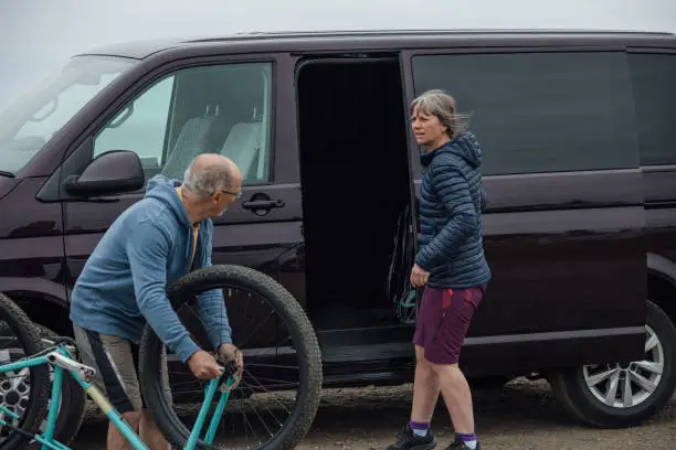 A mature couple wearing mountain biking sports clothing on an overcast day in Alnmouth, Northumberland, Northeastern England. They are getting prepared at their campervan for a day out on their mountain bikes.