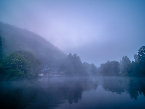Landscape view of misty and foggy atmosphere over a calm lake surrounded by lush green forest