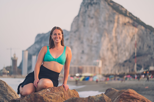 A girl in a green top and black skirt stands on the beach in with Gibraltar and the sea in the background