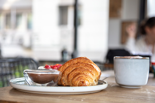 Croissant with fresh coffee standing on coffee shop table.