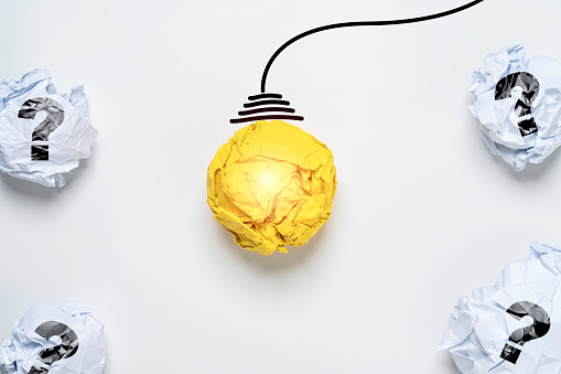 Glowing Yellow scrap paper ball with drawing wire harness among white scrap paper with question mark for creative thinking idea and problem solving solution concept.