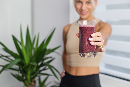 Healthy food concept. Millennial woman in sportswear with glass of fresh smoothie at home, space for text
