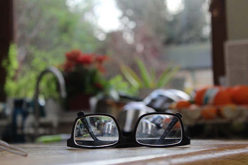 A close up of a pair of black glasses on a wooden surface in a kitchen interior.