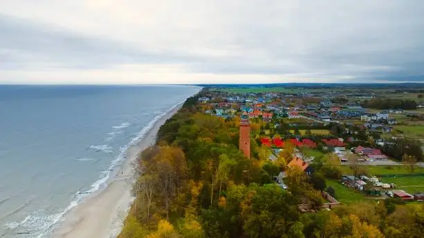 Drone-captured image of Gski Lighthouse, Poland, on a cloudy November day. The serene sea, gentle waves, and empty beach create a tranquil coastal scene, offering a peaceful retreat by the Baltic.