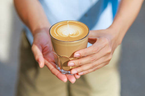 High-angle view of a woman's hand holding a cup of coffee latte, illuminated by soft sunlight.