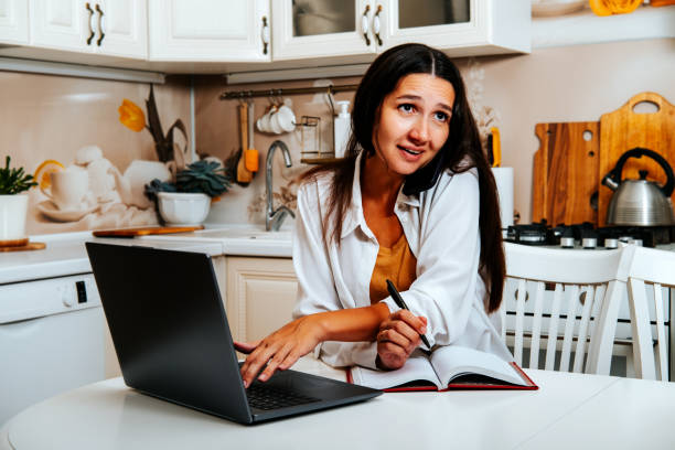 istock Tired woman is working at computer and answering work call at home in the kitchen. 1906947545