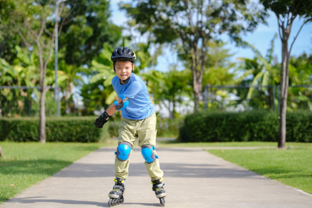 lindo pequeño niño asiático sonriente de 7 años patinando en protección, casco en día soleado de verano - 6 7 years lifestyles nature horizontal fotografías e imágenes de stock