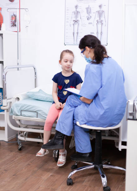 A sweet little girl of Asian decent, who is battling Cancer, stands in her hospital room with her stuffed animal hugged tightly, as she talks with her nurse and patiently waits for her Chemotherapy treatment to run.  She is dressed comfortably in a gown and has a headscarf on to keep her warm.