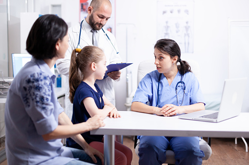 Nurse listening child during consultation in hospital office with doctor taking notes. Healthcare physician specialist in medicine providing health care services treatment examination.