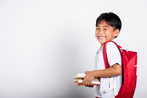 Asian adorable toddler smiling happy wearing student thai uniform red pants stand books for study ready for school isolated on white background, Portrait little children boy preschool, Back to school