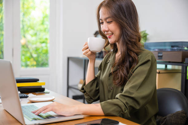 istock Asian young businesswoman drinks coffee sitting desk using laptop keyboard 1907003352