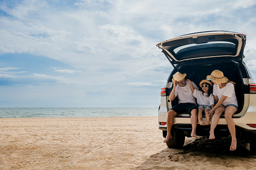 People enjoying road trip sitting down on back their car, Parents and children traveling in holiday at sea beach, family having fun in summer vacation on beach blue sky, Happy Family and World Tourism Day