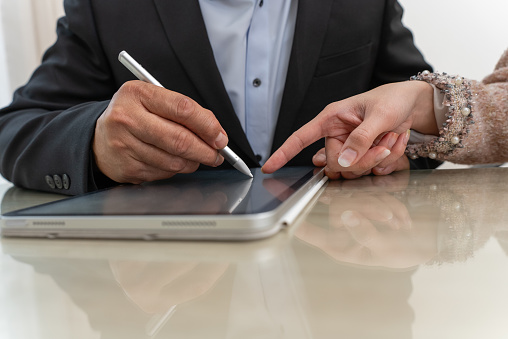 Close-up Hand of businessman in black suit with stylus pen signing contract on digital tablet screen.