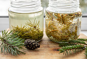 Making syrup of fresh pine needles and spruce needles. Glass jars with needles infused with water in home kitchen.