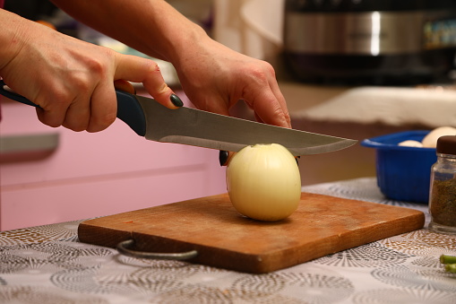 Hands of young female chopping fresh onion on wooden board