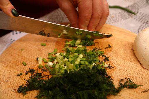 Crop anonymous female chef in uniform cutting fresh green parsley with knife on cutting board