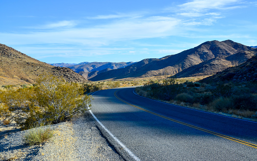 Empty asphalt road in the desert, Mountains in the background in Joshua Tree National Park, CA