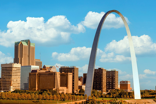 St. Louis Gateway Arch and downtown cityscape at sunset with a partly cloudy blue sky.