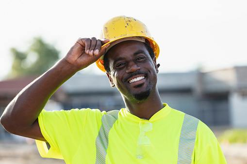 Headshot of an African-American construction worker wearing reflective clothing and putting on a hardhat. He is smiling at the camera.